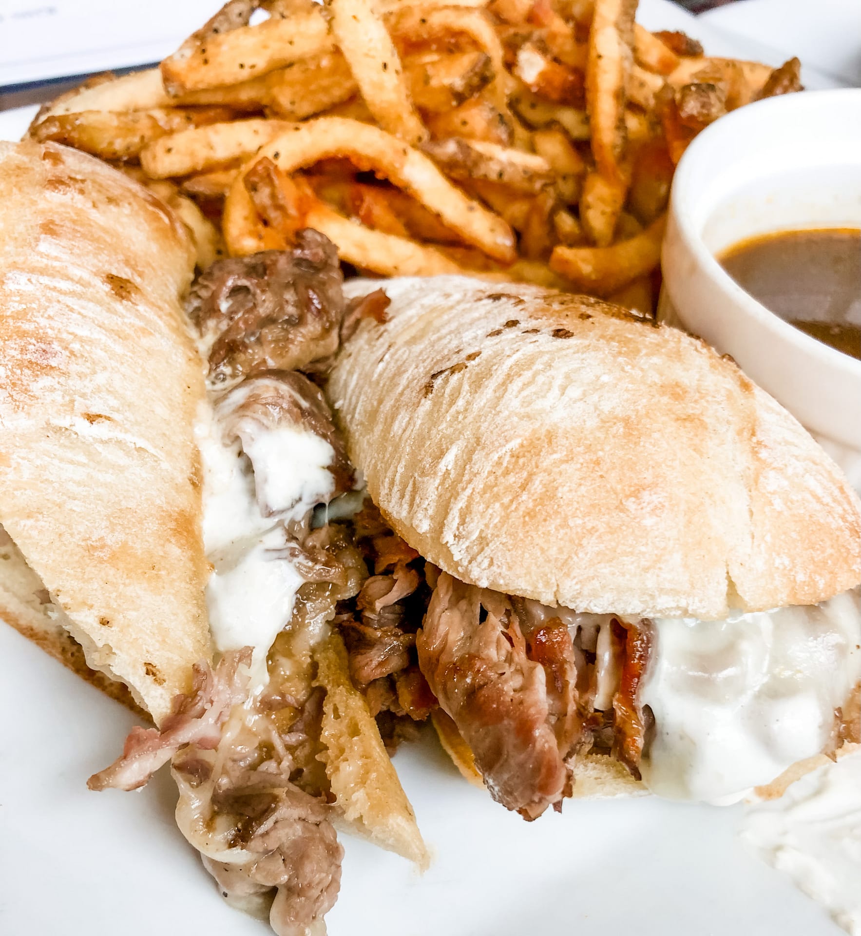Plate with steak sandwich and french fries with sauce on the side