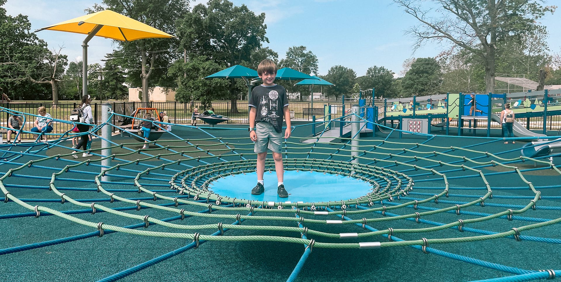 Happy boy standing in the middle of a playground rope web