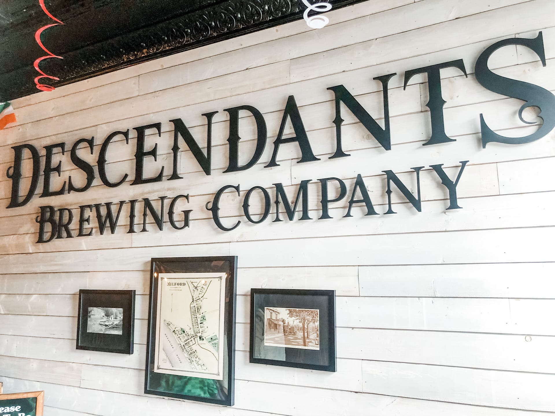 Descendants Brewing Company sign with black letters and white wood in background 