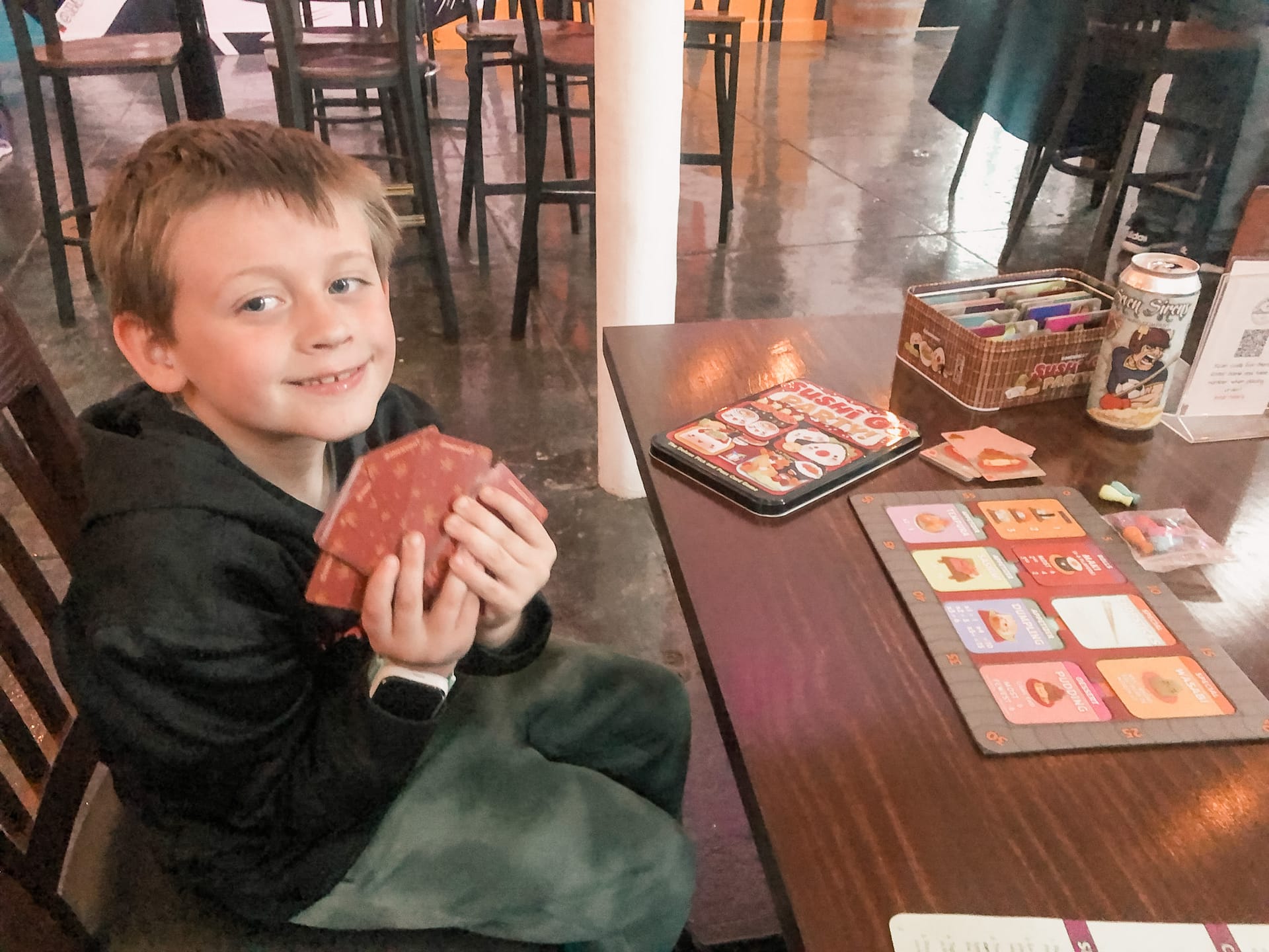 Happy boy sitting down holding a set of Go Sushi Party cards