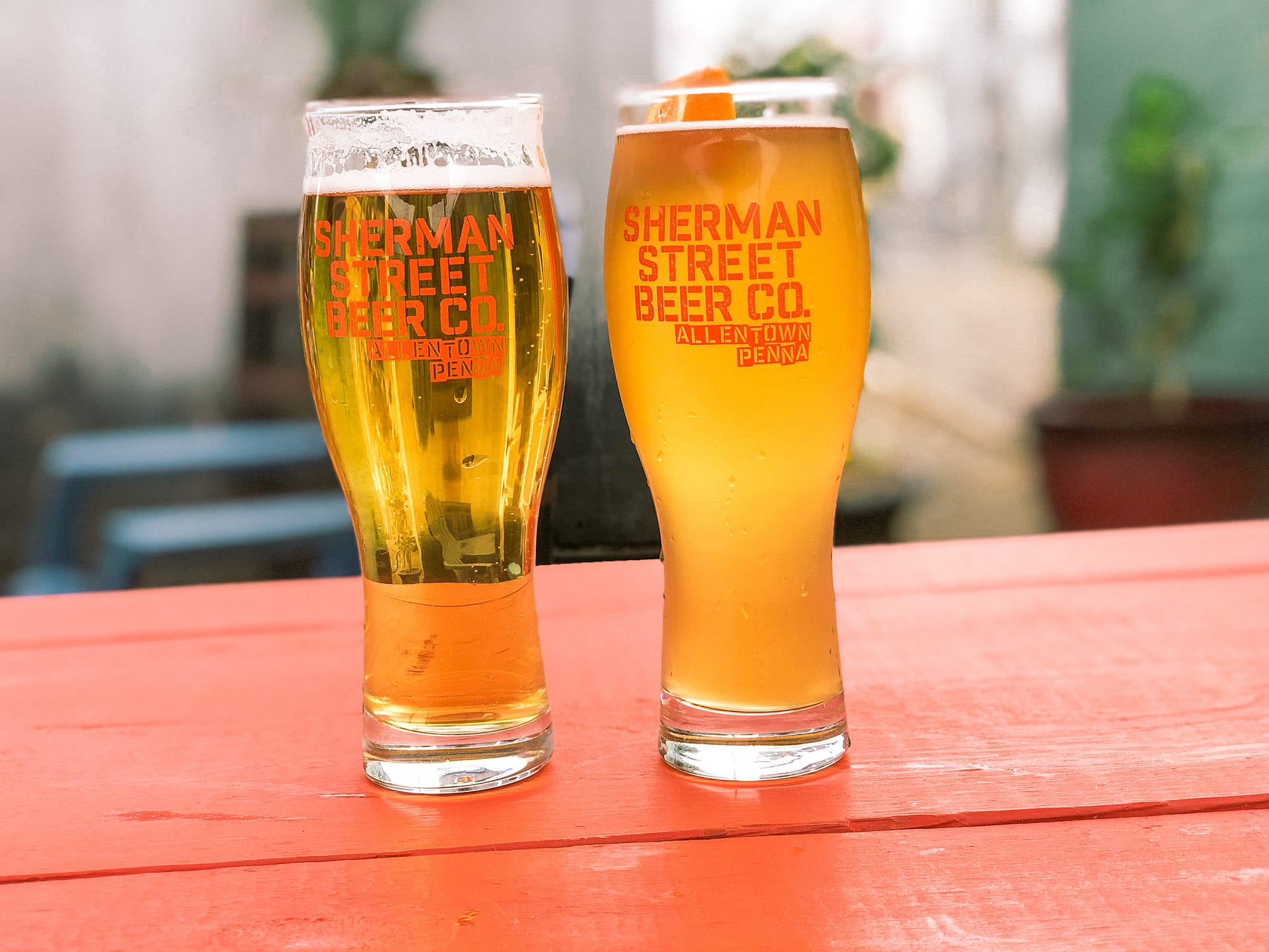 Two glasses of beer placed on a red table and glass reads Sherman Street Beer Co.