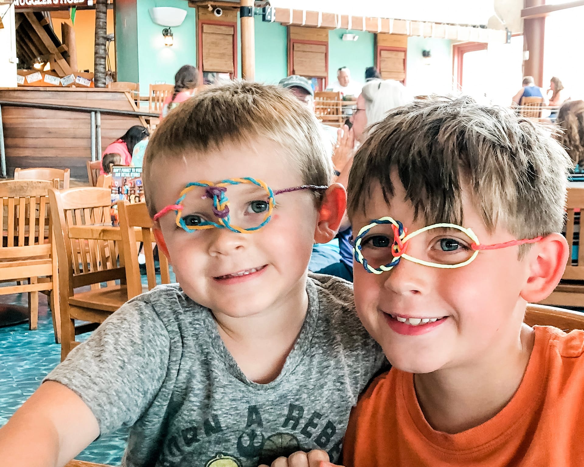 Two happy boys inside a restaurant wear hand made colorful glasses