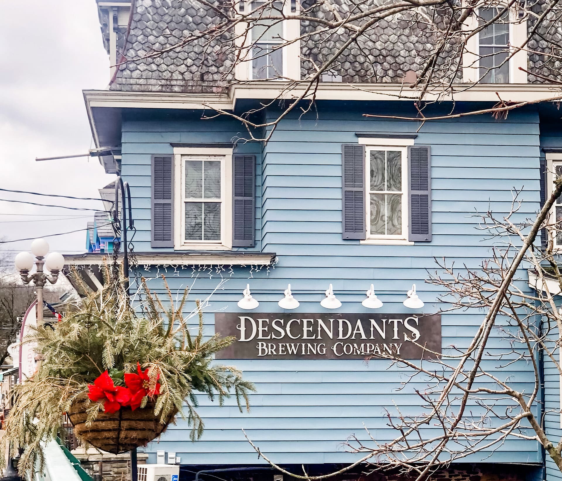 Outside of colonial blue building sign hanging reads Descendants Brewing Company