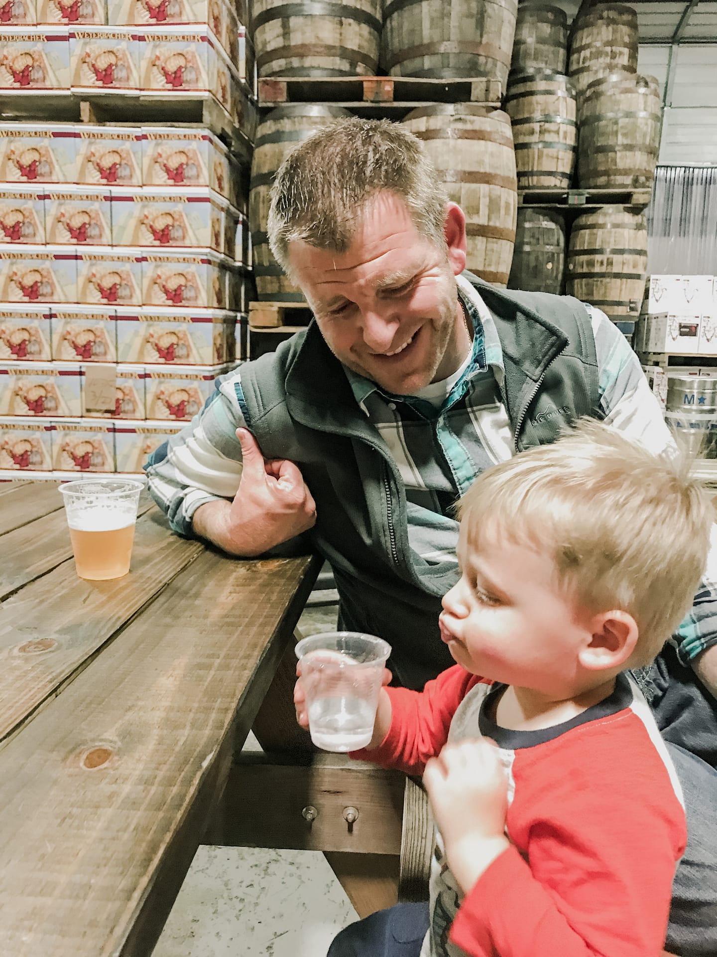 Happy father looking at son's puffed up checks while drinking water both sit at a picnic table with boxes in background