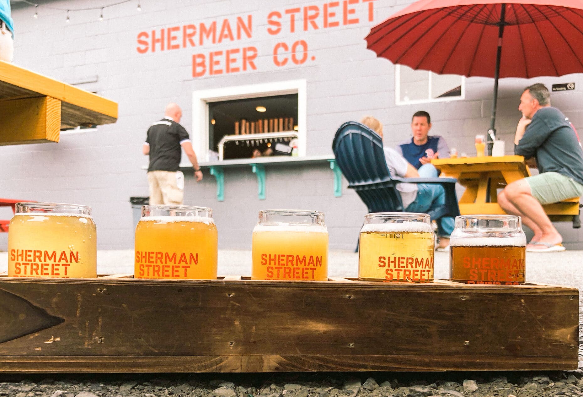 Beer flight with Sherman Street Beer Co. sign and garden in background