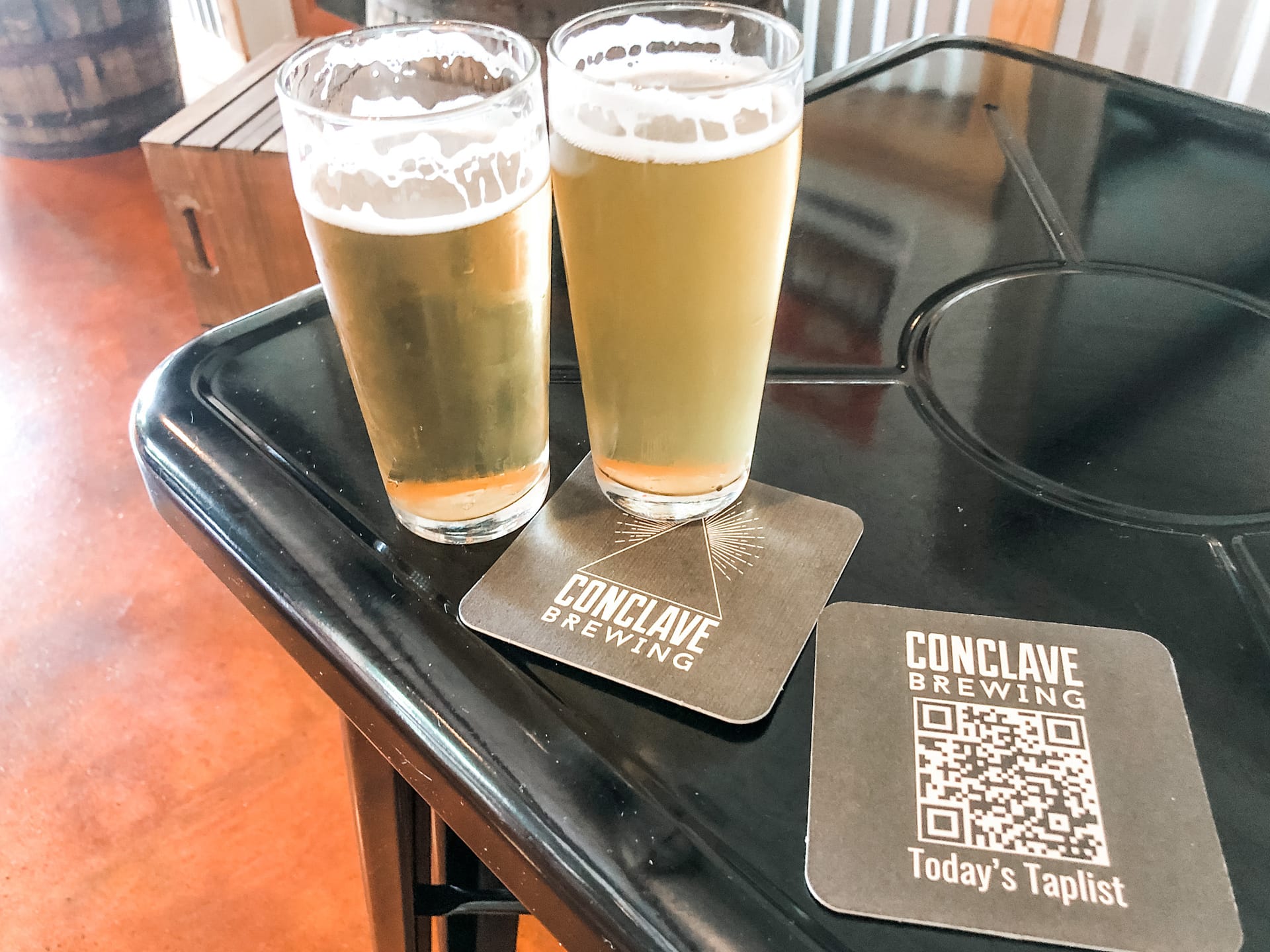 Two glasses of beer with coaster that reads Conclave Brewing